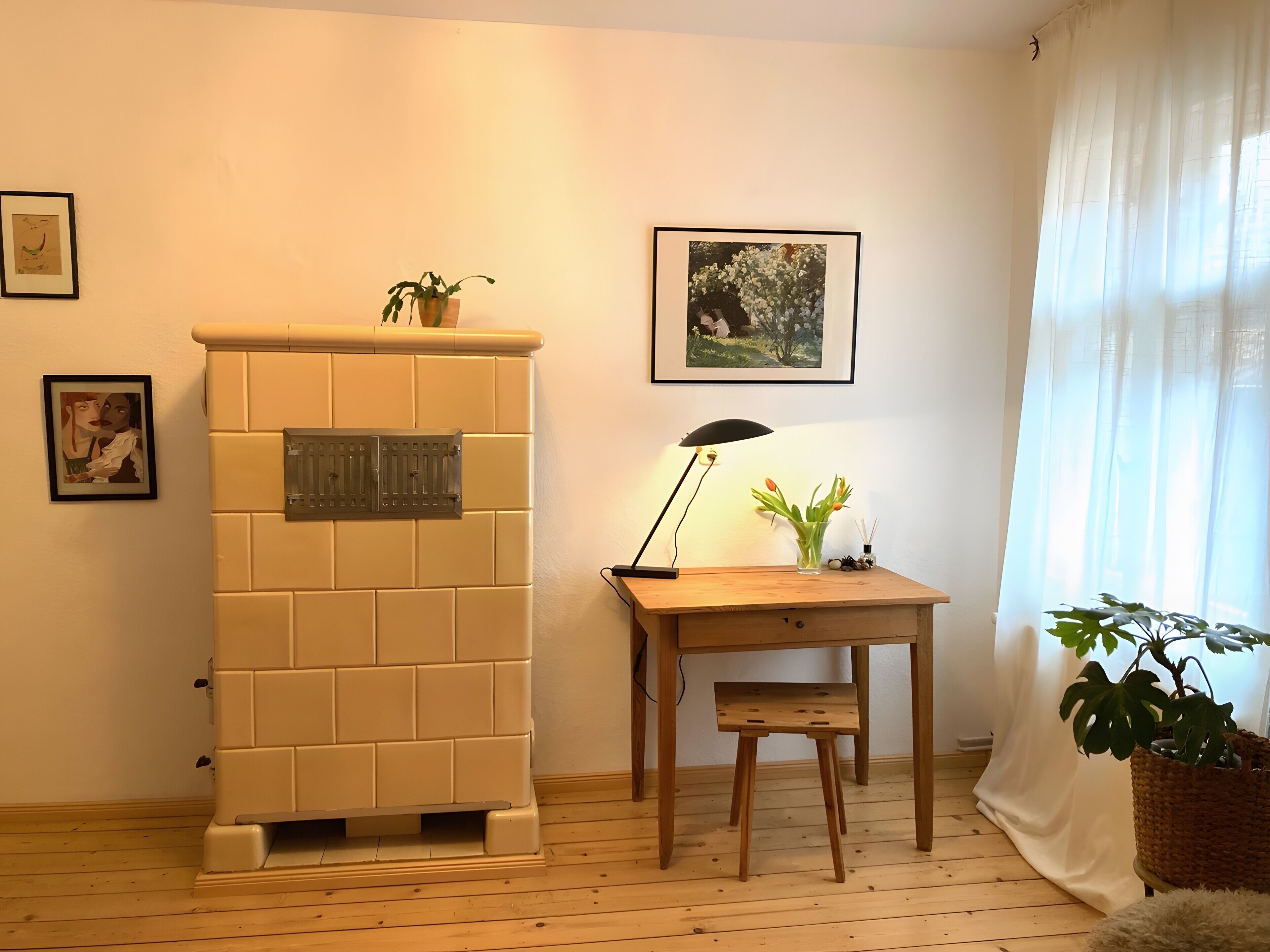 A room with a tiled fireplace, a wooden desk with a lamp, a small stool, and a potted plant.