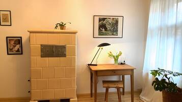 A room with a tiled fireplace, a wooden desk with a lamp, a small stool, and a potted plant.