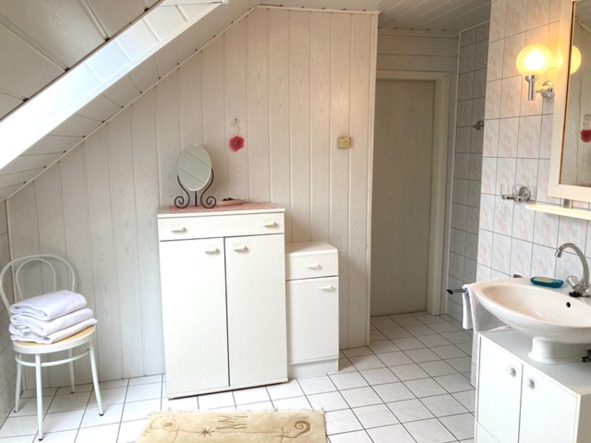 A small, white, sloped-roofed room with a vanity, mirror, and sink.