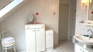A small, white, sloped-roofed room with a vanity, mirror, and sink.