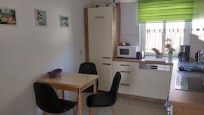 A small kitchenette with a microwave, toaster, and coffee maker. There is a dining table with two chairs and a small basket on it.