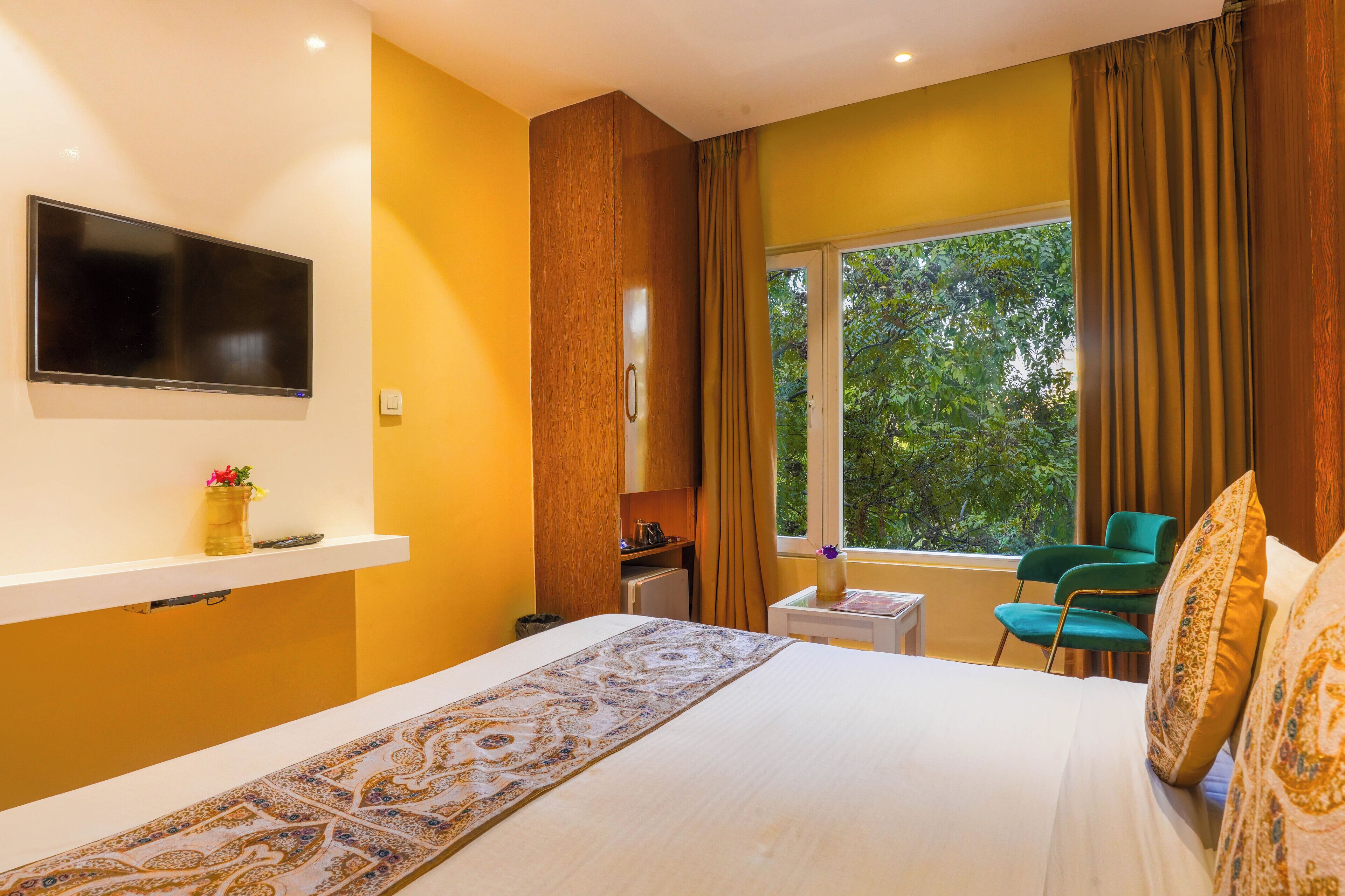 A hotel room with a bed, a TV mounted on the wall, a small table, a chair, and a window with curtains.