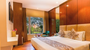Ein geräumiges Schlafzimmer mit einem großen Bett, Holzvertäfelung, Blick auf Grün und einer kleinen Sitzecke mit einem Sessel.