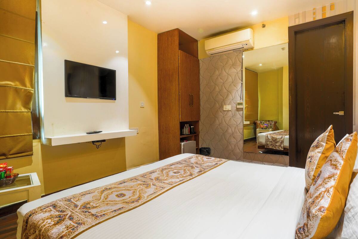 Una camera d'albergo con un letto, una TV a parete, un armadio e uno specchio che riflette l'ambiente.