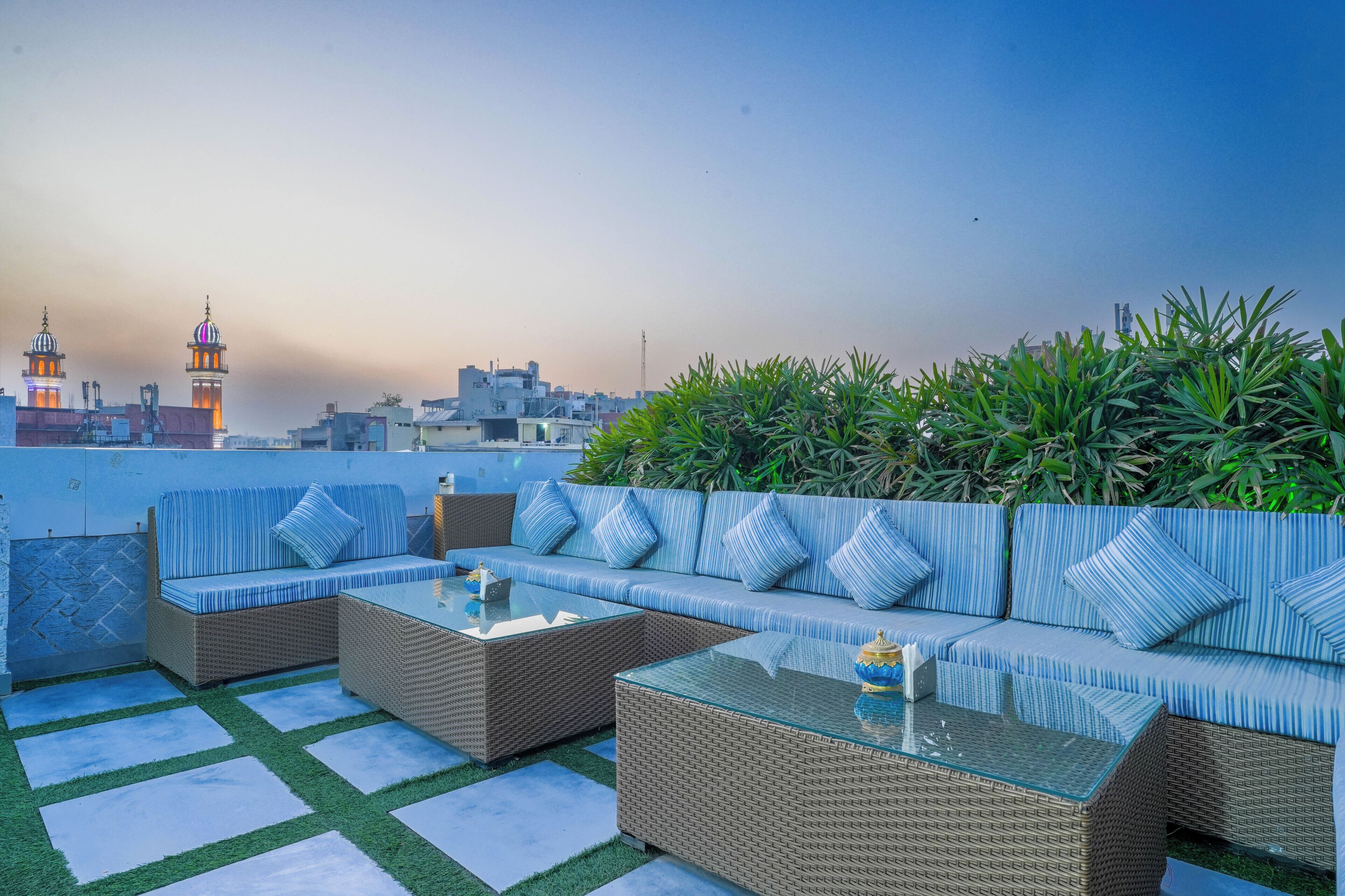 A rooftop terrace with wicker furniture and a glass table, overlooking a cityscape with buildings and a mosque.