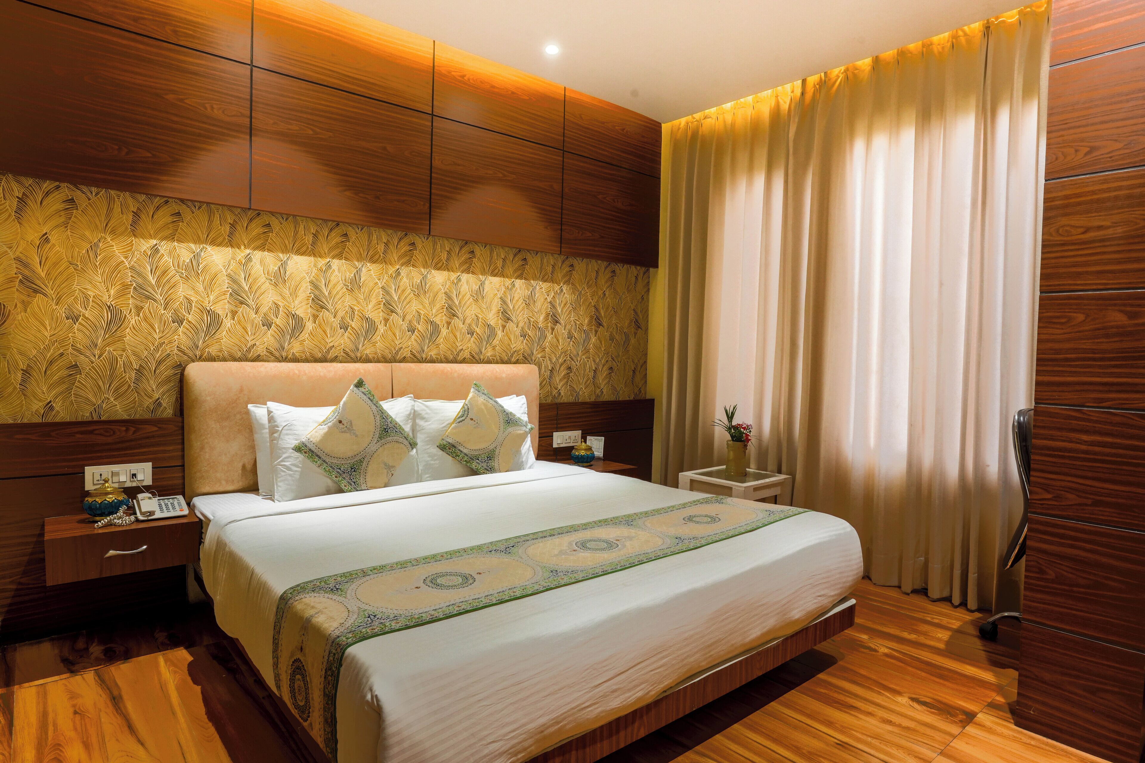 A hotel room with a large bed, wooden headboard, and a nightstand with a phone and a vase.