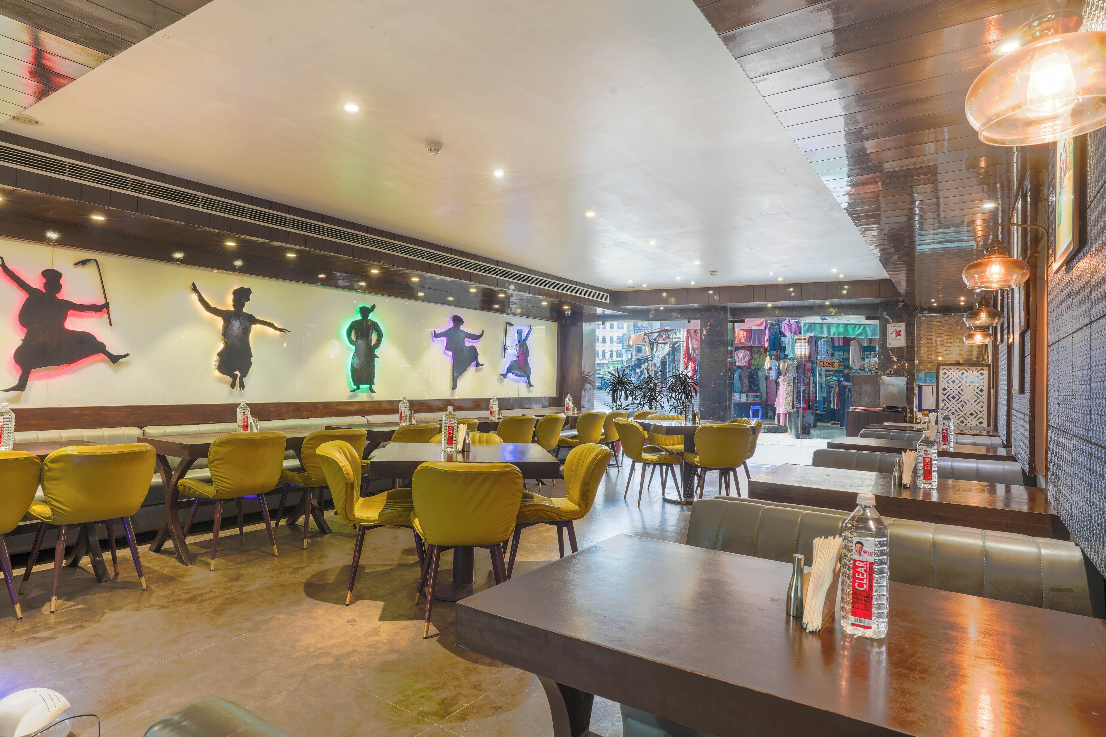 Un restaurante con sillas y mesas amarillas, un techo alto y arte mural que representa bailarines.
