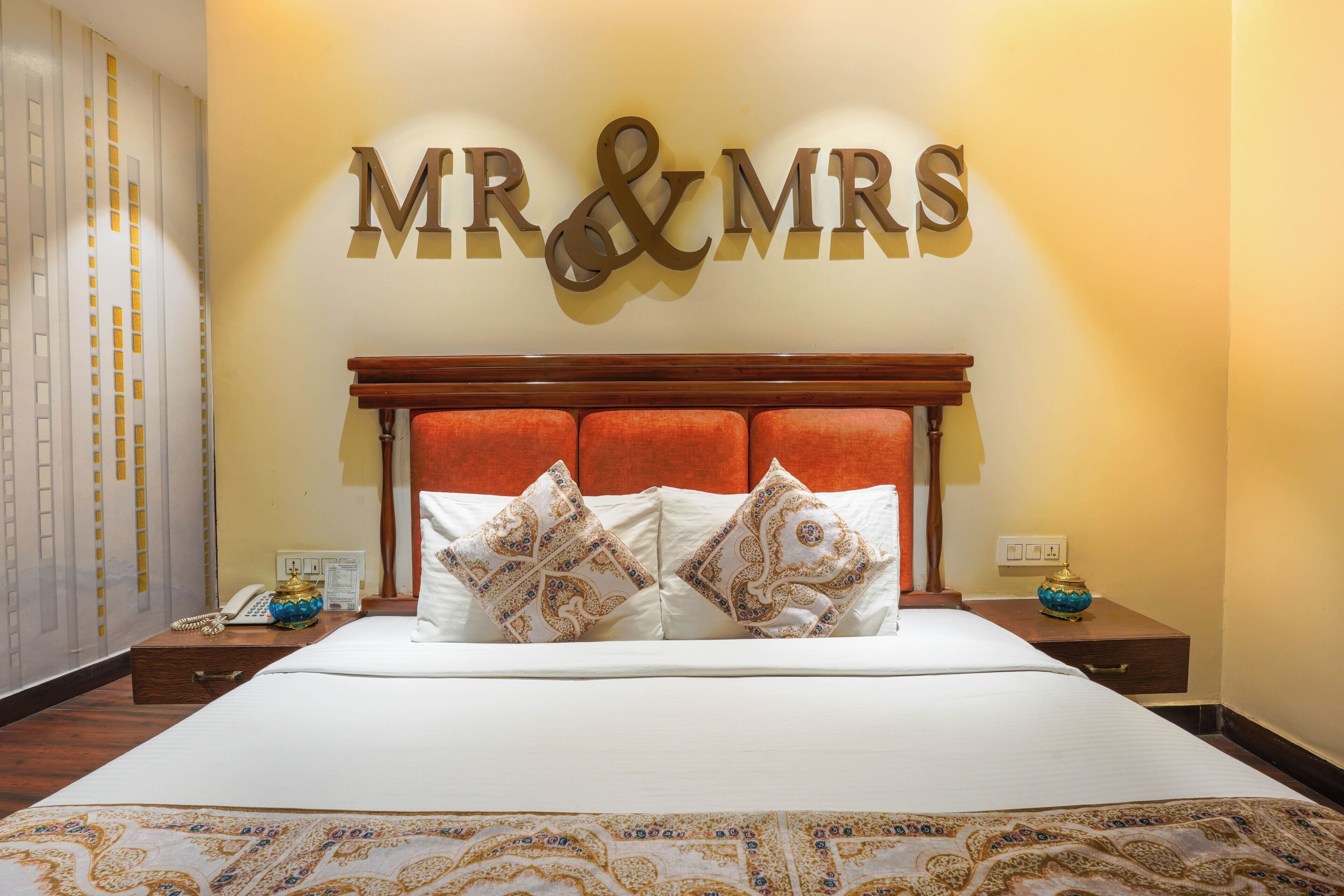 A hotel room with a large bed, two nightstands, a wooden headboard, and a wall sign reading "MR & MRS".