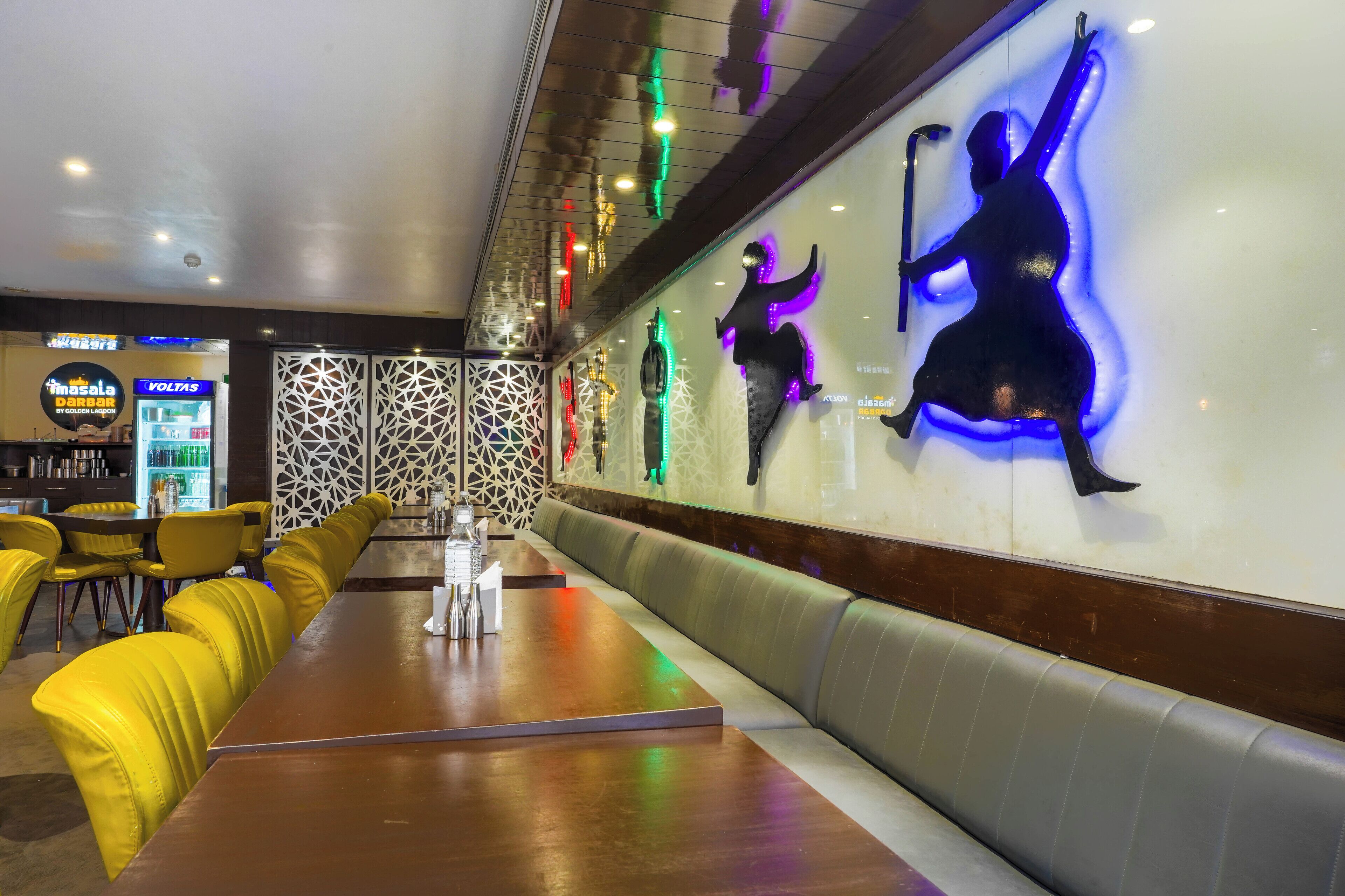 A restaurant interior with a long counter, yellow chairs, and a decorative wall with illuminated figures.