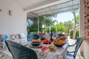 A dining table set outdoors with a view of trees, a bench with cushions, and a patterned tablecloth.