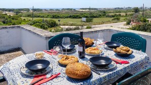 Mesa posta ao ar livre com comida, vinho e uma vista panorâmica.