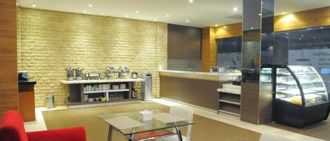 Interior moderno de una cafetería con mostrador, zona de estar y vitrina.