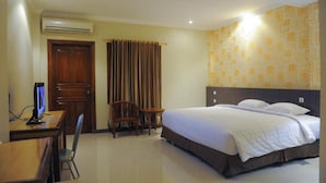 Een hotelkamer met een bed, een bureau met een computer, een stoel en een raam met gordijnen.