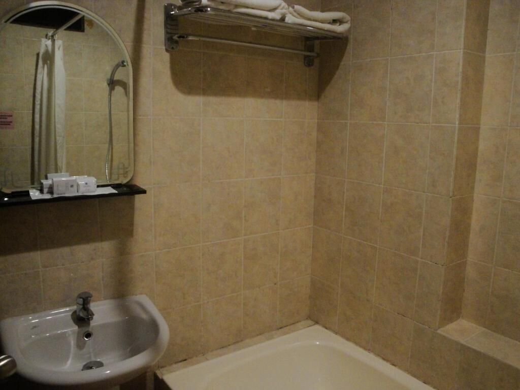 A bathroom with a sink, mirror, shower, and towel rack.