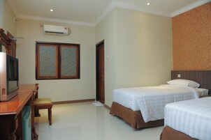 Una habitación de hotel con dos camas, un escritorio con televisor y un equipo de aire acondicionado en la pared.