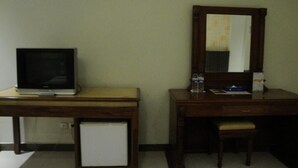 Een kleine hotelkamer met een houten bureau, een televisie, een spiegel en een koelkast.