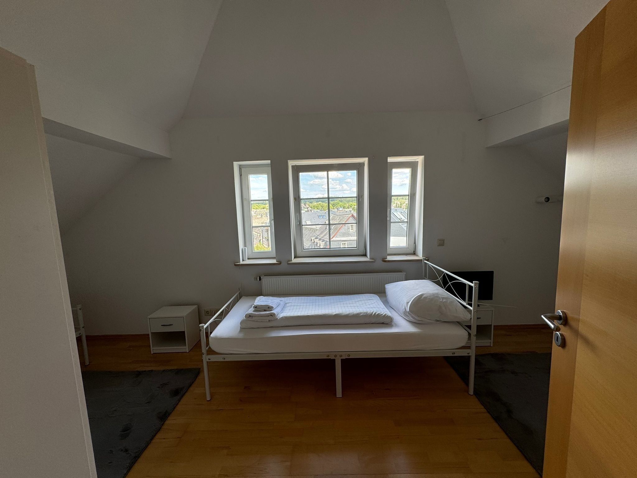 A small, single-bed room with a sloped ceiling, a radiator, and three windows providing natural light.