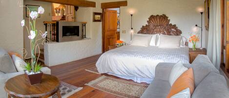 A bedroom with a large bed, a sofa, a small table with a plant, and a TV on the wall.