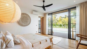 A bedroom with a bed, a ceiling fan, a large window, and a view of the outdoors.