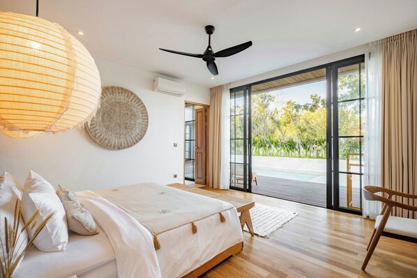 Une chambre à coucher avec un lit, un ventilateur de plafond, une grande fenêtre et une vue sur l’extérieur.