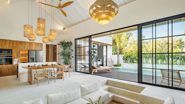 A modern open-plan living area with a kitchen, dining space, and a large sliding glass door leading to a pool.