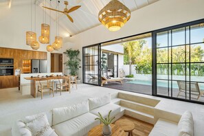 Un espacio habitable moderno y abierto con cocina, comedor y un gran ventanal corredero que da a una piscina.