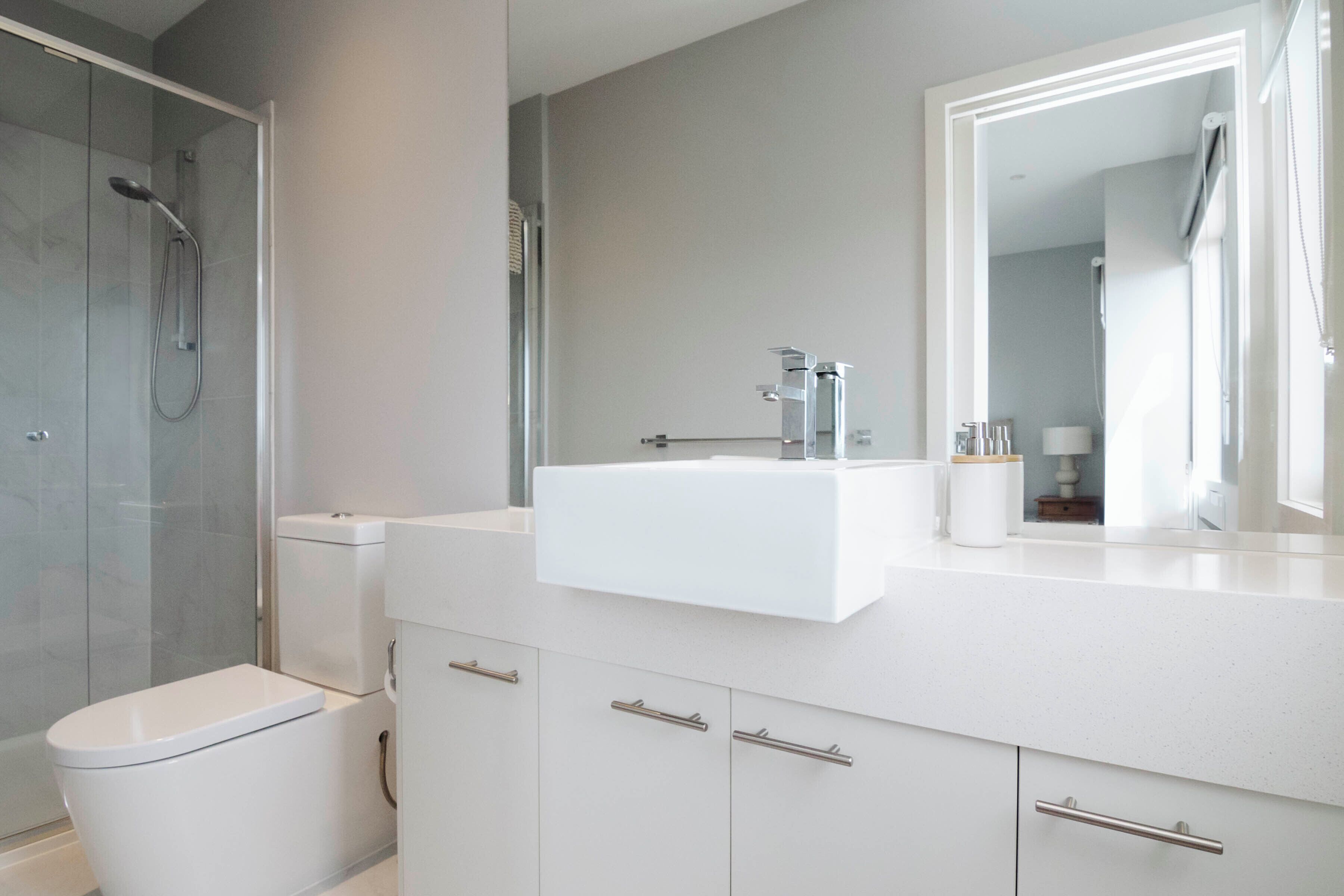 A modern bathroom with a glass-enclosed shower, a white toilet, and a vanity with a mirror and sink.