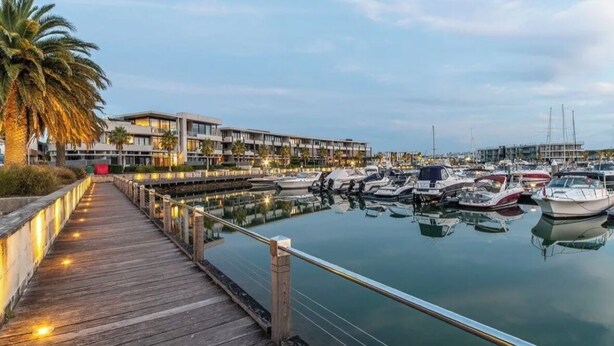 Un puerto deportivo con barcos amarrados, un muelle de madera y edificios modernos al fondo.