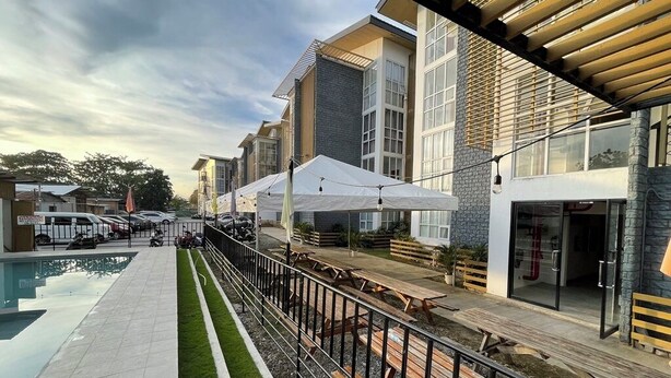 A poolside area with outdoor seating and umbrellas, a building with large windows, and a clear sky. - Melce Place Studio Unit Condo (Lapu-Lapu City)
