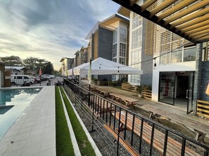Ein Poolbereich mit Sitzgelegenheiten und Sonnenschirmen, ein Gebäude mit großen Fenstern und ein klarer Himmel.