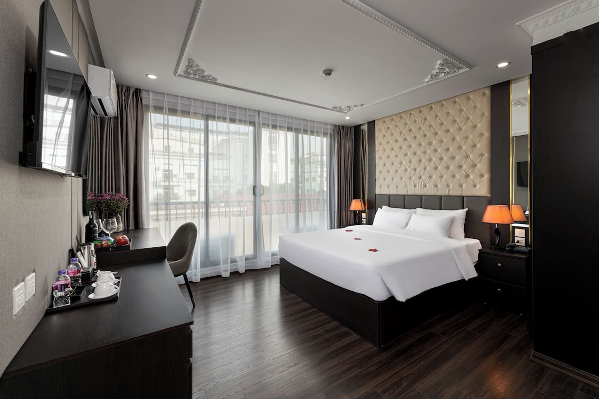 Een hotelkamer met een groot bed, een bureau met stoel, een televisie en een raam met gordijnen.