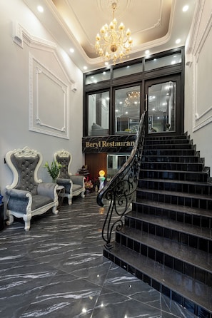 Una imponente escalera conduce a un restaurante con suelo de mármol y sillas ornamentadas.