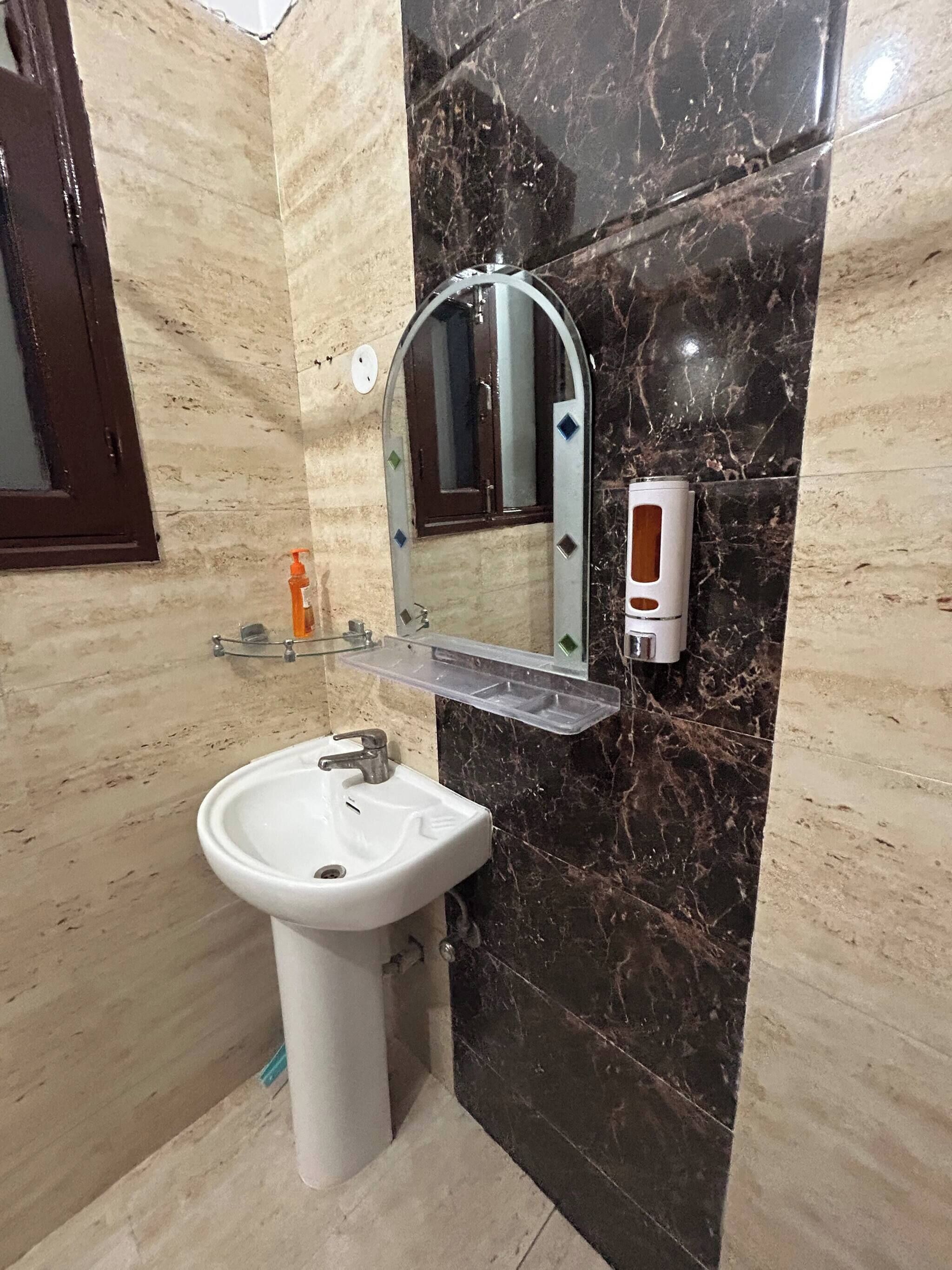 A bathroom with a white sink, a mirror, and a soap dispenser.