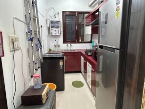 A compact kitchen with a refrigerator, stove, sink, and a small trash bin. - Entire 3bhk Luxury Flat in Zirakpur-panchkula-chandigarh-mohali, Punjab, India (Dera Bassi)