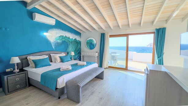 Een slaapkamer met een bed, nachtkastjes, een bureau en uitzicht op zee door een glazen deur.