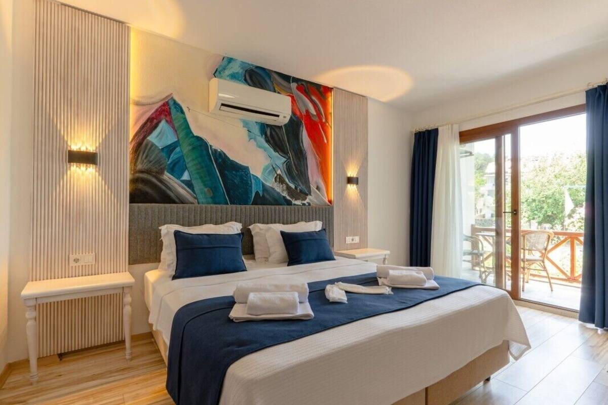 A modern hotel room with a large bed, a painting on the wall, and a balcony with a view.