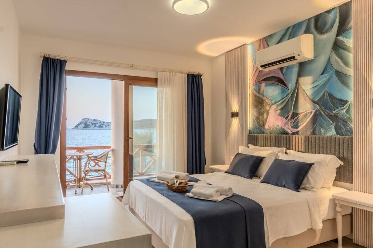 A hotel room with a bed, a desk, a chair, and a view of the sea.