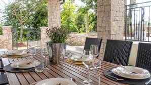 Un área de comedor al aire libre con un pilar de piedra, barandilla de metal y una mesa preparada para cuatro, con platos, vasos y cubiertos.
