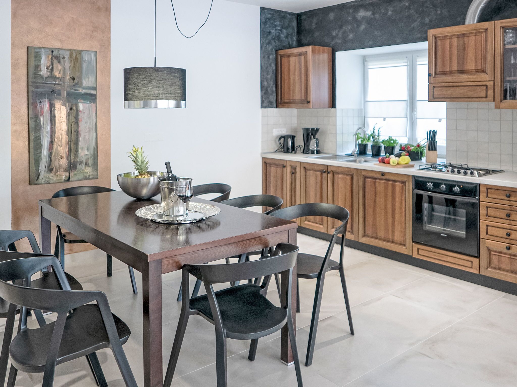Una cocina moderna con armarios de madera, una mesa de comedor con sillas, una lámpara colgante y un ventanal que proporciona luz natural.