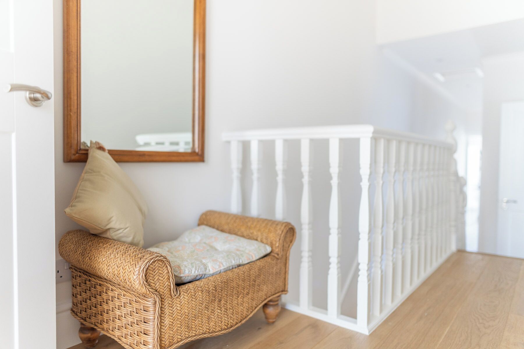 A wicker chair with a cushion, a white railing, and a mirror on the wall.