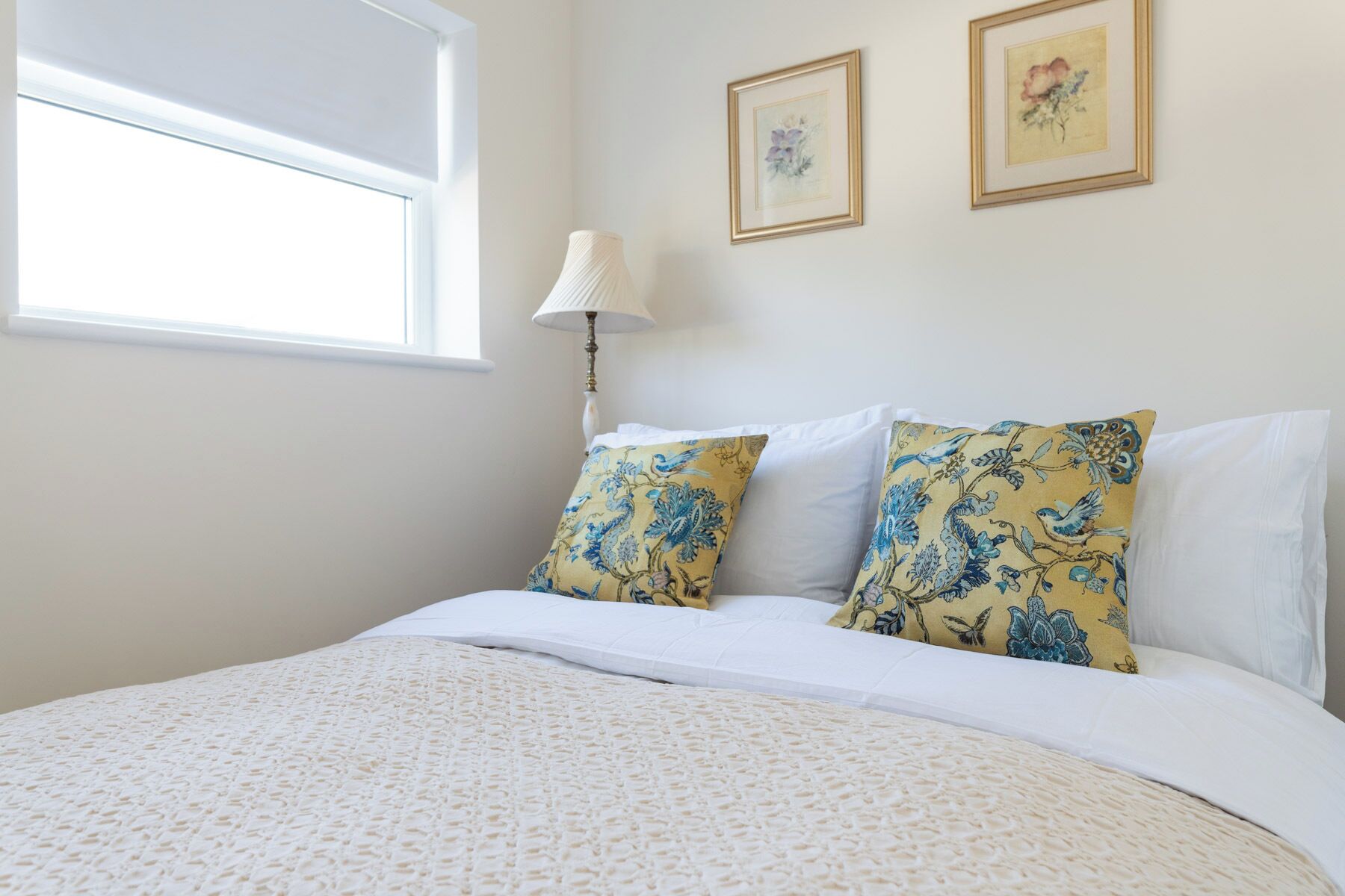 A bedroom with a bed, two pillows, a lamp, and two framed pictures on the wall.