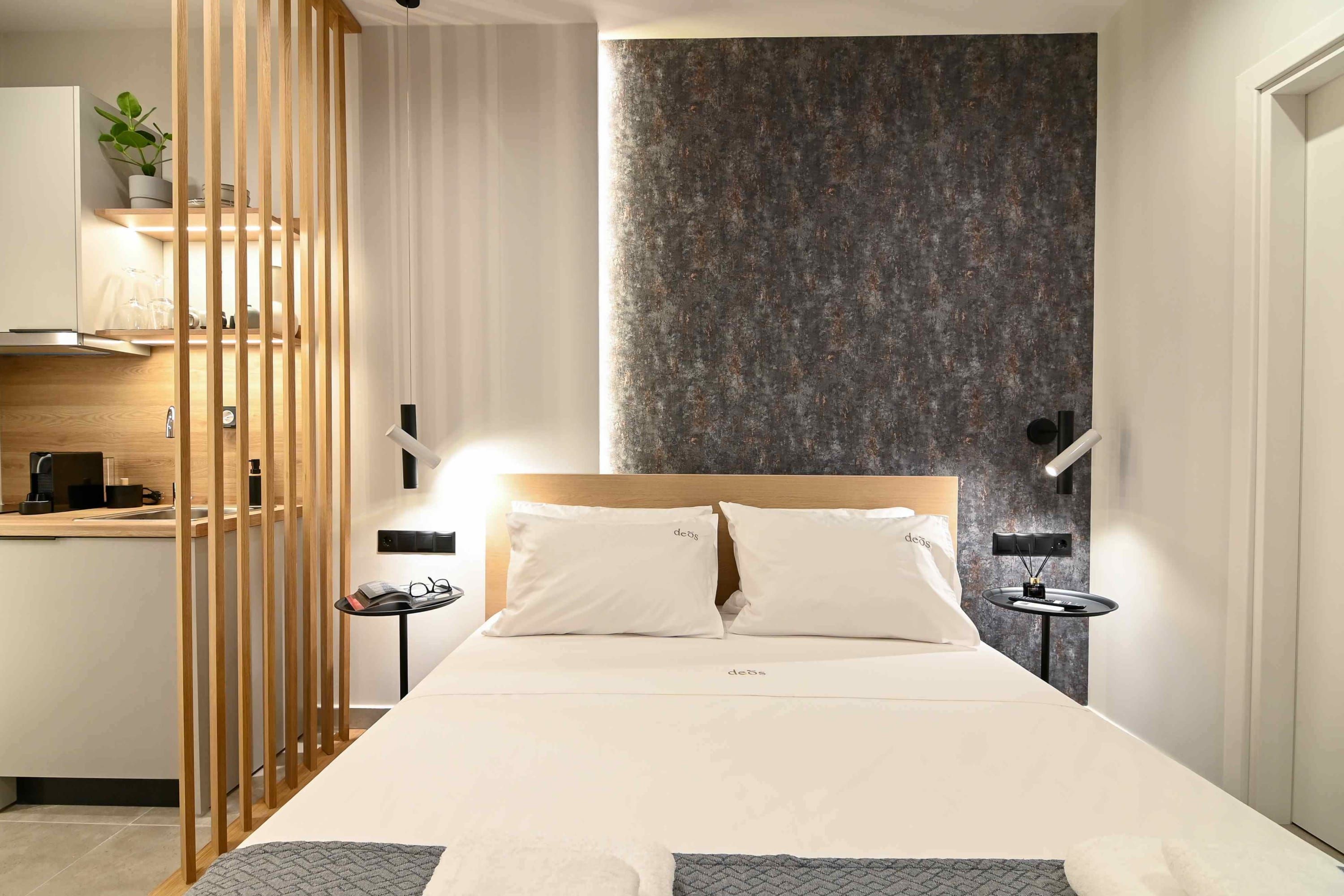 Un dormitorio moderno con cabecera de madera, cama con sábanas blancas, una mesita de noche con lámpara y estante de pared con una planta.