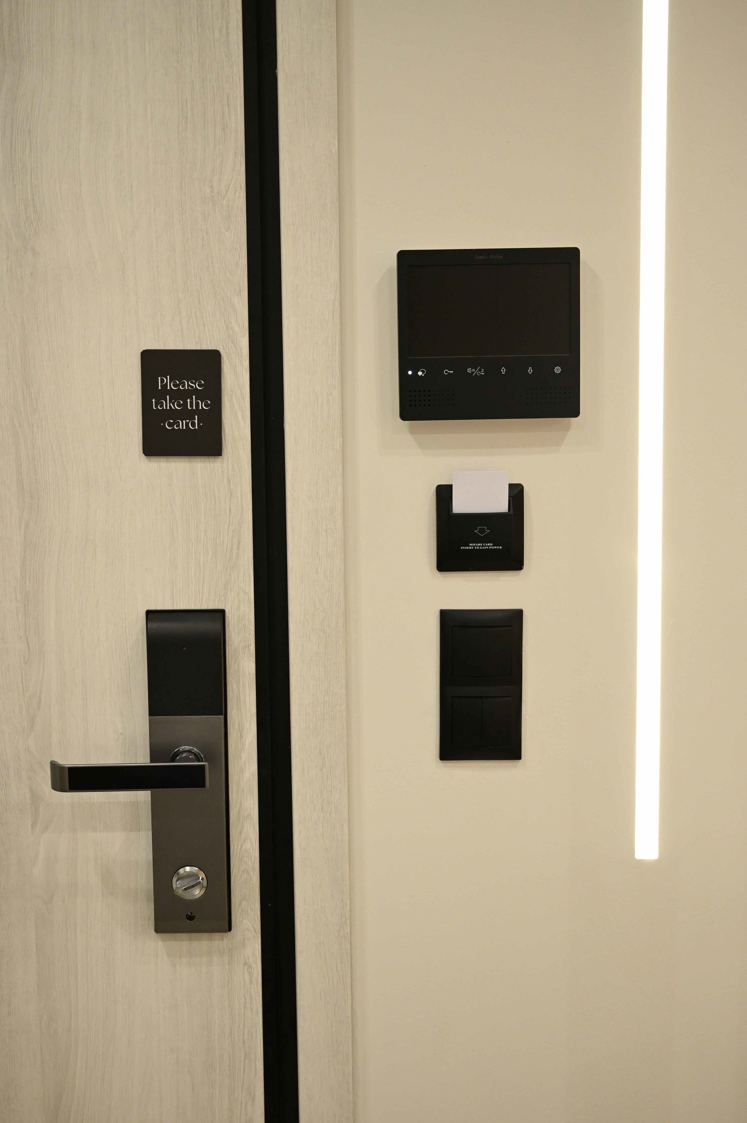 A modern door with a card reader, a sign instructing to take the card, and a wall-mounted control panel.