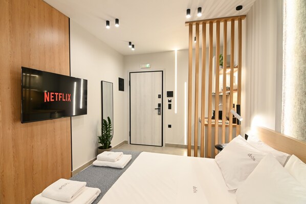 A hotel room with a bed, a TV mounted on the wall, a wooden partition, and a door leading to a bathroom.