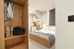 Una habitación de hotel con una cama de madera, un armario con ropa colgada, un escritorio pequeño y una mesita de noche.