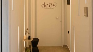 A hallway with a door labeled "deos" and a small table with a plant and a vase. - Deos living experience 1 (Athina)