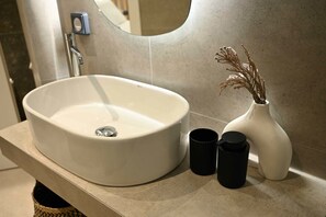 Une salle de bain avec un lavabo blanc, un miroir et un vase contenant des plantes séchées.