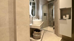A modern bathroom with a round sink, a mirror, a shower enclosure, and a built-in shelf with a decorative item. - Deos living experience 1 (Athina)