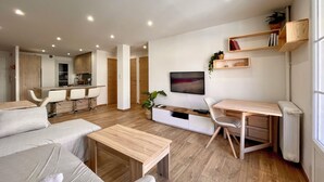 Ein modernes Wohnzimmer mit einer Couch, einem Couchtisch, einem Fernseher und einem Essbereich mit Stühlen und einem Tisch.