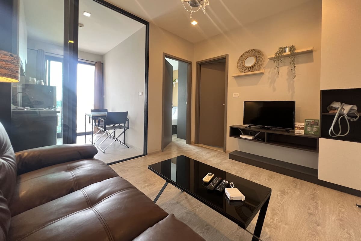 A modern living room with a leather sofa, a glass coffee table, a flat-screen TV, and a dining area with a table and chairs.